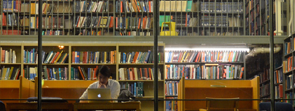 Usuario en biblioteca leyendo en un ordenador